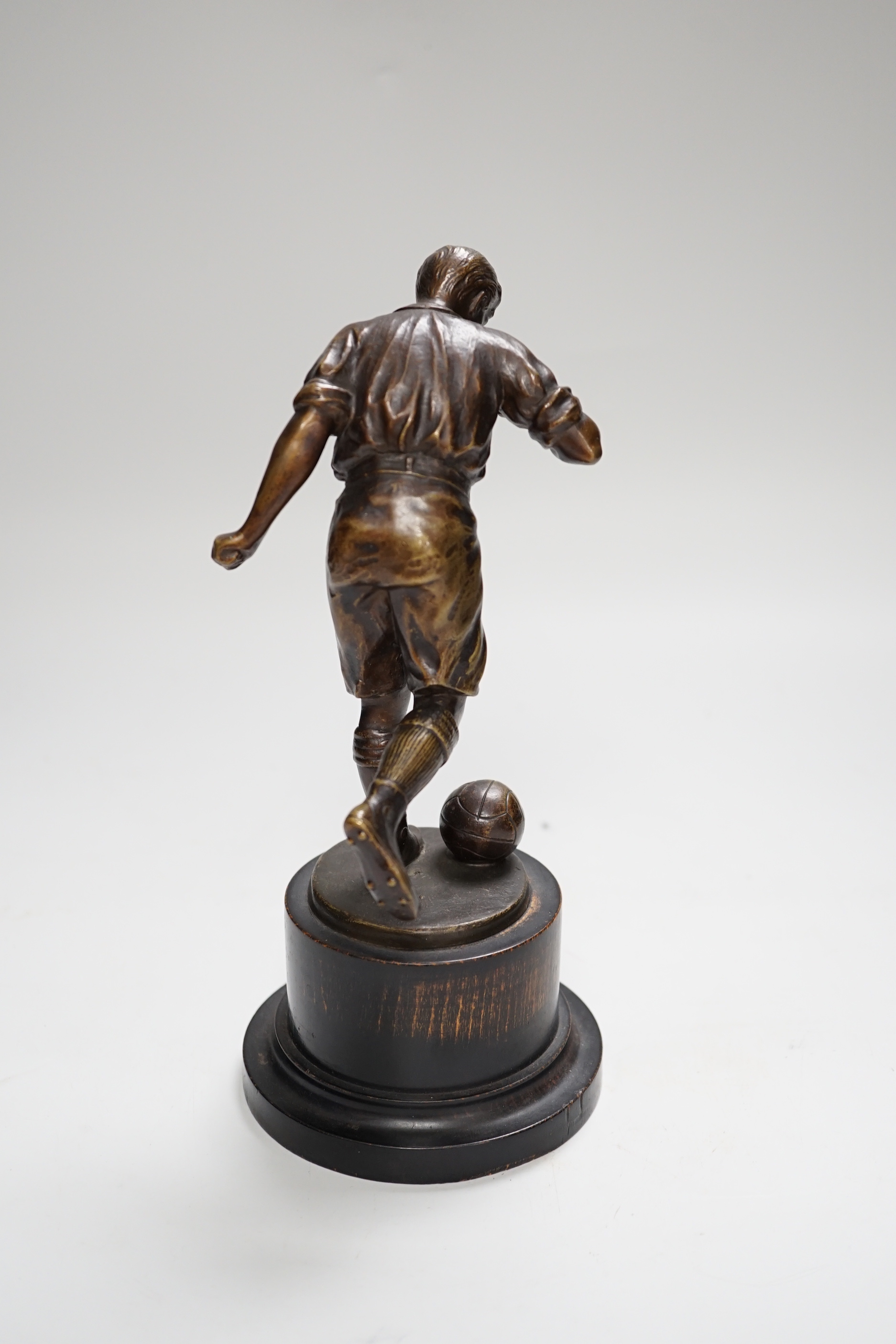 A pre-war bronze figure of a footballer, raised on a circular ebonies wood base, 23cm high